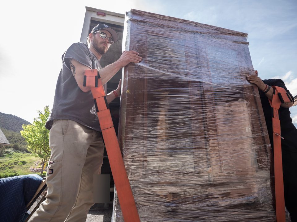 Two of the crew lifting a wrapped armoire off the truck